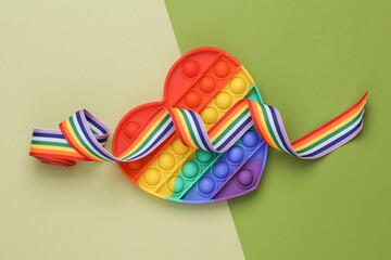 Pop it antistress toy in the shape of a heart with a rainbow lgbt ribbon on a green background. Top view