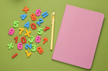 Notebook and lot of colored plastic numbers on a green background. Education. Top view