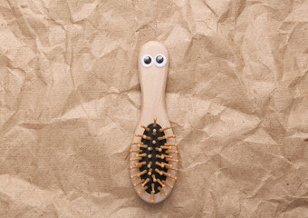 Wooden hair brush with eyes on craft crumpled paper background. Eco concept