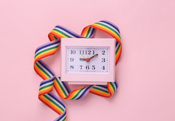 Clock wrapped with lgbt rainbow tape on a pink background