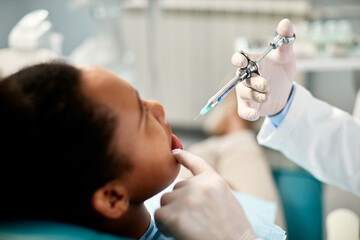 Close up of dentist gives anesthetic to black female patient during dental procedure.