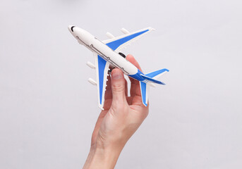 Air travel. Tourism concept. Hand holds miniature of passenger plane on gray background