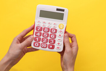 Female hands hold a white calculator with pink buttons on a yellow background