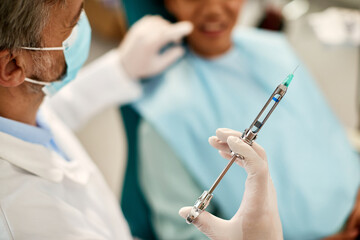 Close up of dentist using syringe with anesthetic during dental appointment with patient.