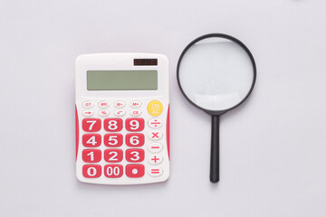 Calculator with a magnifying glass on a gray background. Business concept.