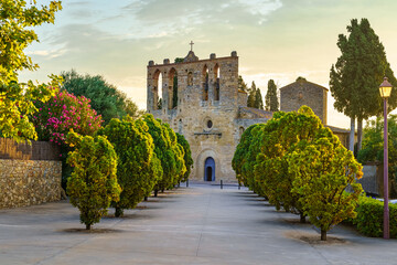 Old stone church with walk with trees at sunset in the town of Peratallada, Girona, Spain.