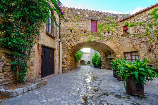 Picturesque alley with stone arches and the sun appearing between the houses at dawn, Peratallada, Girona, Spain.