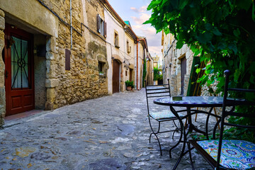 Fototapeta na wymiar Nice alley full of stone houses and iron table and chairs to rest, Peratallada, Girona, Spain.