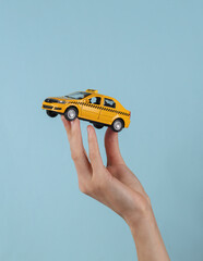 Mini model yellow taxi car in female hand on a blue background.