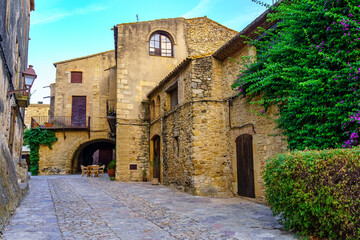 Naklejka premium Medieval stone houses with green vines at sunset on a summer day, Peratallada, Girona, Catalonia.