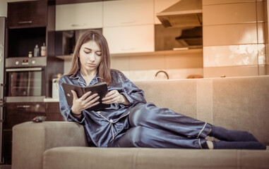 Young woman in nightie reads book while lying on the sofa in living room