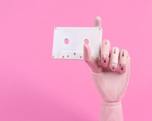 Wooden hand holding audio cassette on pink background