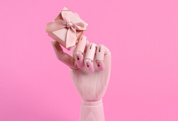 Wooden hand holding gift box on pink background