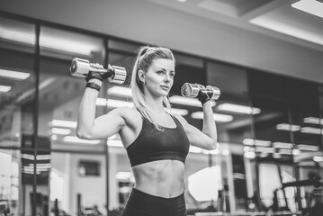 Fototapeta na wymiar Sexy young fit woman with perfect body dressed in sportswear trains shoulder muscles with dumbbells in modern gym. Healthy lifestyle
