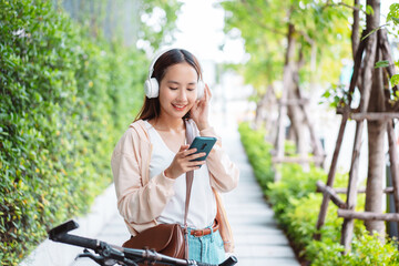 Fototapeta na wymiar Happy Asian young woman listen music headphone with bicycle using mobile phone in park, street city her smiling using bike of transportation, ECO friendly, People lifestyle concept..