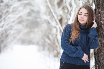 A young girl in a winter park on a walk. Christmas holidays in the winter forest. The girl enjoys winter in the park.