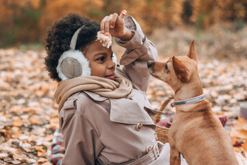 Cute African-American girl plays with a dog on a picnic in the autumn park.Diversity,autumn concept.Selective focus.