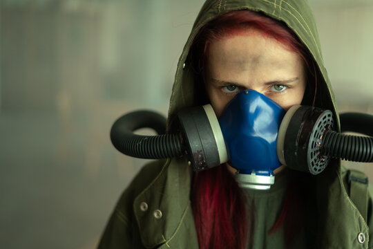 Young pandemic survivalist woman in gas mask looking in front of her on the background with apocalyptic war area around. Sad woman in breathing oxy mask