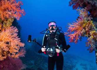 Obraz na płótnie Canvas An underwater photographer holding her camera swimming between some beautiful vibrant colored soft coral