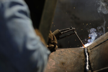 Shallow depth of field (selective focus) details with a professional welder welding an industrial metallic pipeline.