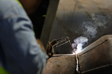 Shallow depth of field (selective focus) details with a professional welder welding an industrial metallic pipeline.