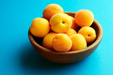 Bright ripe apricots in a wooden bowl on a blue background