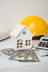 Construction drawings with helmet, money and model of house, cost of building. Vertical image