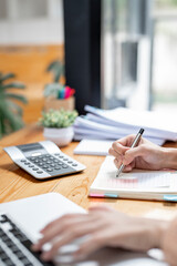 Cropped shot of woman hand writing note with pen on notebook and paperwork while sitting at desk office, vertical view.