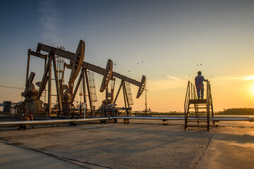 Silhouette of oil workers working in oil rig or oil fields and gas station in the evening with beautiful sunset.
