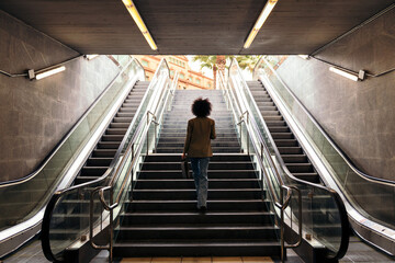 rear view of the silhouette of an unrecognizable business woman walking up the stairs of the subway station with a briefcase in her hand, concept of urban lifestyle and growth - Powered by Adobe