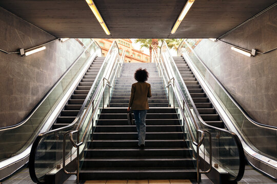 rear view of the silhouette of an unrecognizable business woman walking up the stairs of the subway station with a briefcase in her hand, concept of urban lifestyle and growth