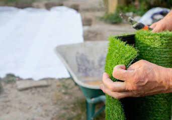 A dirty working hand unrolls the artificial grass. A man will lay an artificial lawn on a geotextile.