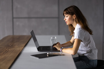 Smiling young woman typing on her laptop in kitchen