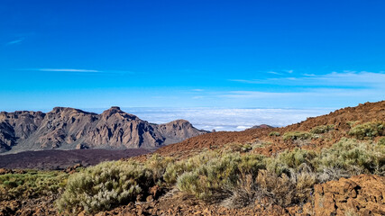 Fototapeta na wymiar Hiking trail over volcanic terrain leading to summit of volcano Pico del Teide, Mount Teide National Park, Tenerife, Canary Islands, Spain, Europe. Valley and Atlantic Ocean is covered with clouds