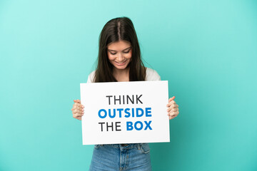 Young caucasian woman isolated on blue background holding a placard with text Think Outside The Box