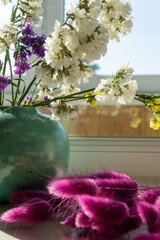 Dry flowers in turquoise ceramic round vase on the windowsill. Purple lagurus in the front. 