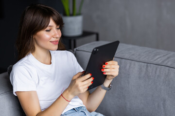 Young woman using tablet sitting on sofa at home at living room