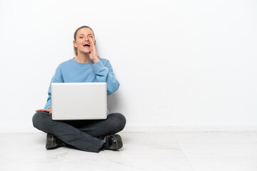 Young woman with a laptop sitting on the floor shouting with mouth wide open