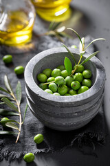 Green and small raw olives with mortar and a twig.