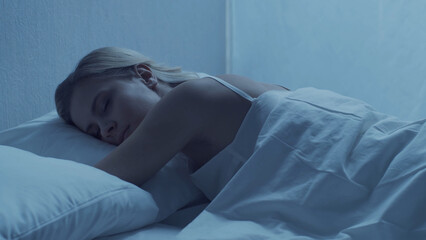Young woman lying in the bed at night. Beautiful blond sleeping girl. Twilight in the bedroom,...