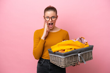Young caucasian woman holding a clothes basket isolated on pink background with surprise and...