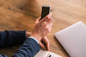 Blank black screen phone in male hand. Working space at home or office. Caucasian man plan and noted schedule (holiday trip) on the diary at office desk. Calendar for planner concept.