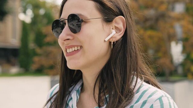 Footage of young casual woman using earpods and answering at phone call.