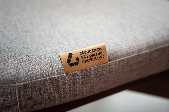 "PET Plastic upcycling" product label tag on the sofa seat fabric material part. Sign and symbol object photo, selective focus.