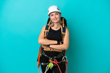 Young caucasian rock climber woman isolated on blue background looking up while smiling