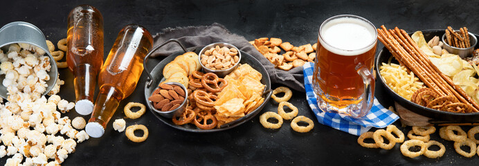 Assortment of beer and salty snacks on dark background.