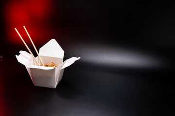 Asian food: wok pasta, spaghetti, with vegatables in white box. black isolated. wooden chopsticks. Concept of production of paper containers for fast food. Red backlight. Copy space