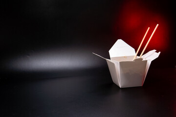 Asian food: wok pasta, spaghetti, with vegatables in white box. black isolated. wooden chopsticks. Concept of production of paper containers for fast food. Red backlight