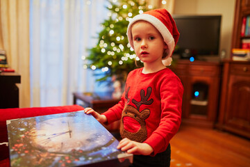 Adorable little preschooler girl wearing holiday sweater and red Santa hat decorating Christmas tree