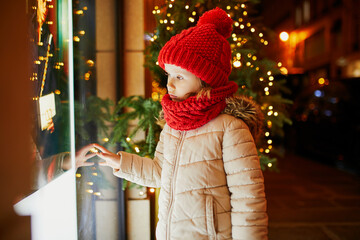 Preschooler girl looking at window glass of large department store decorated for Christmas
